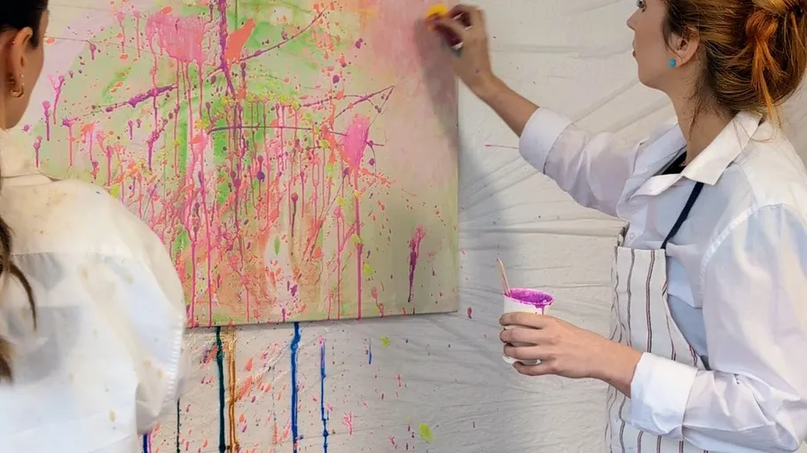 Two women creating abstract painting on canvas.