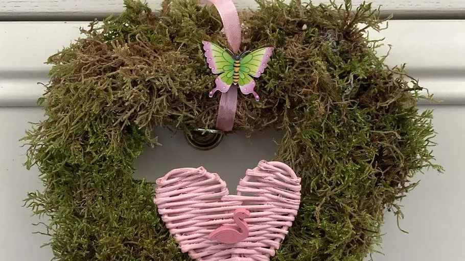 Moosherzkranz mit rosa Schmetterlingsdekoration.