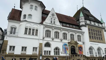 Historisches Gebäude mit Rundbogenfenstern und Bannern.