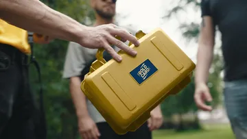 Hand holding a yellow box outdoors.