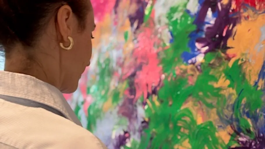 Woman observing colorful abstract painting closely.