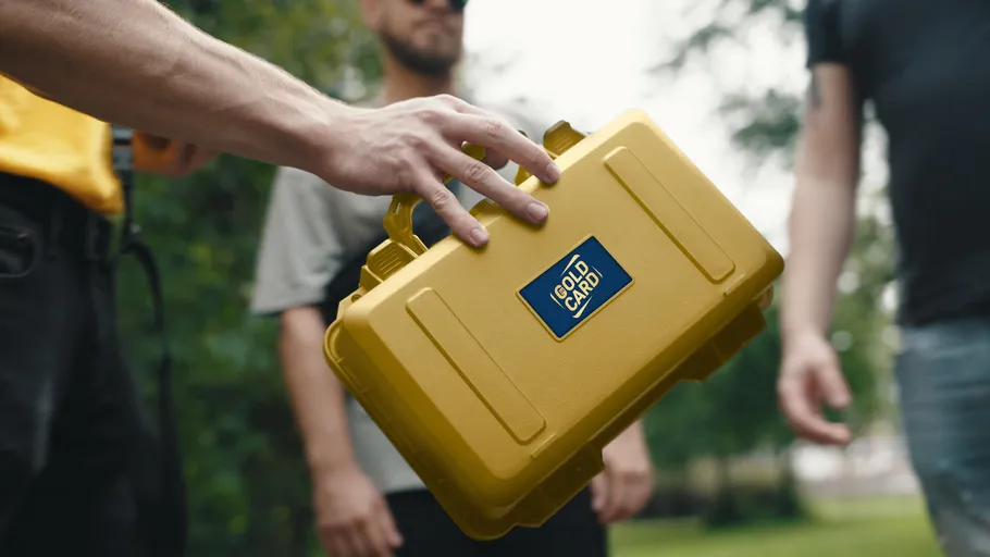 Hand holding yellow case with logo outdoors.