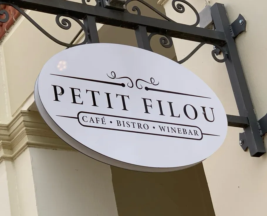 Ovals Schild mit 'PETIT FILOU' vor Café.