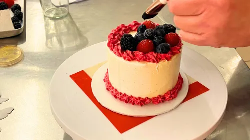 Hand decorates cake with berries on table.