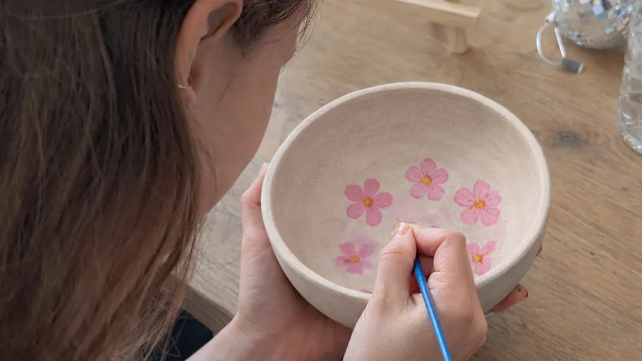 Person painting flowers inside a ceramic bowl.
