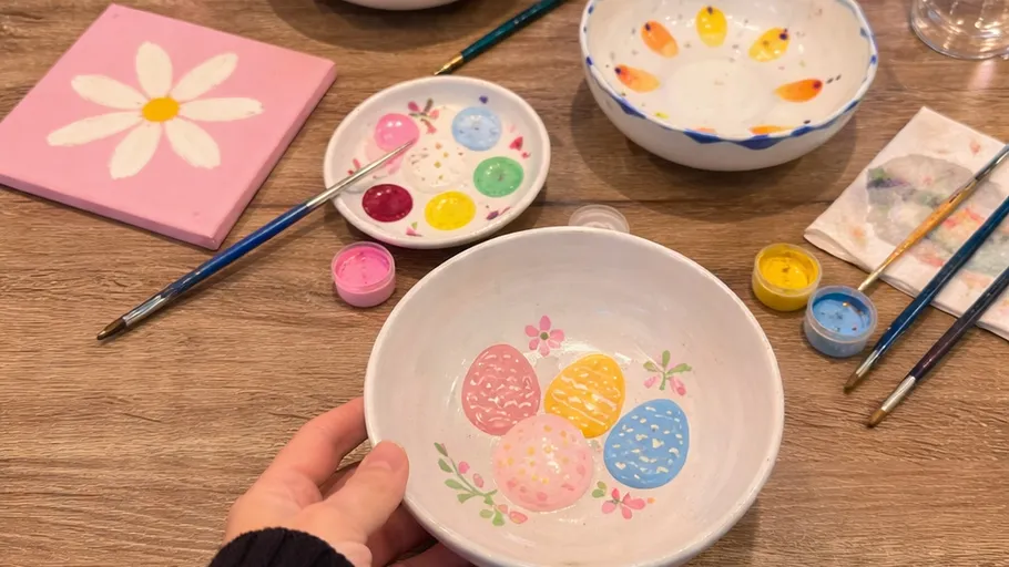 Hand holds painted bowl with colorful eggs.