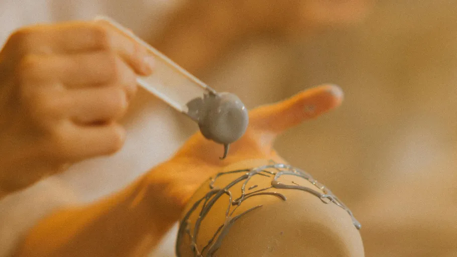 Hands applying glaze to pottery with brush.