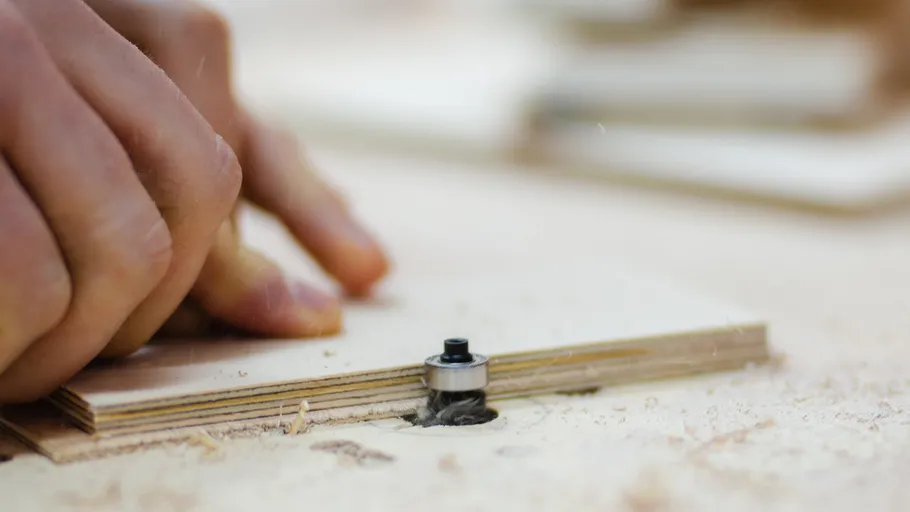 Hände arbeiten mit Holz und Fräswerkzeug.