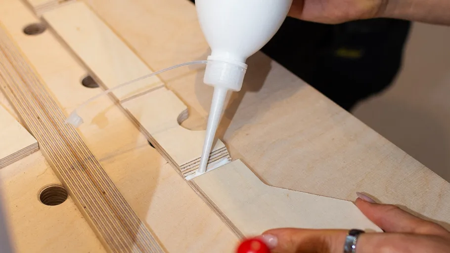 Person gluing wooden parts together on workbench.