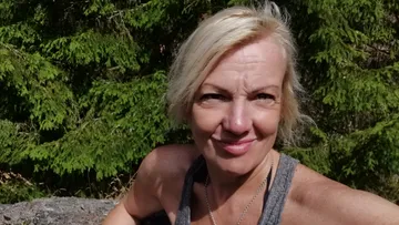 Lächelnde Frau im Freien nahe grüner Bäume.