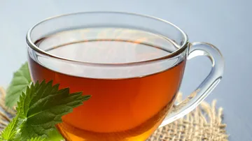 Glass cup of tea with leaves nearby.