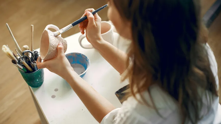 Person painting a ceramic mug at a table.
