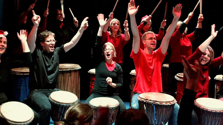 Group of people drumming enthusiastically on stage.