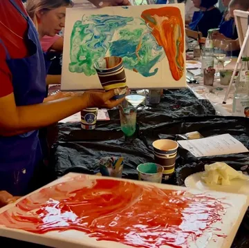 Artist holds colorful abstract painting in workshop.