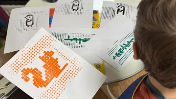 Child observing pixel art on printed sheets.