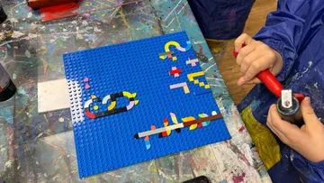 Child creating art with LEGO on blue board.