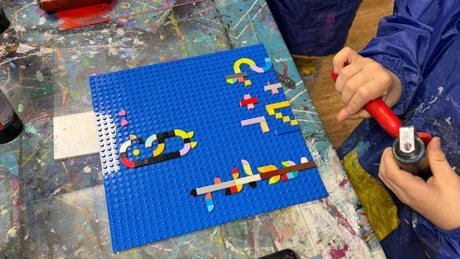 Kind erstellt Kunst mit LEGO auf blauer Platte.