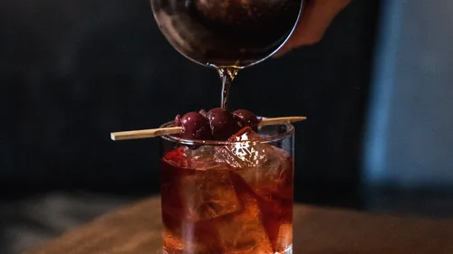 Cocktail being poured with cherries garnish.