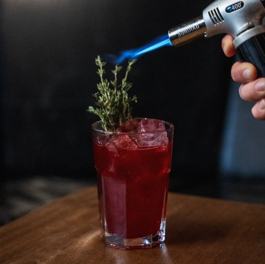 Red cocktail with herbs being flamed.