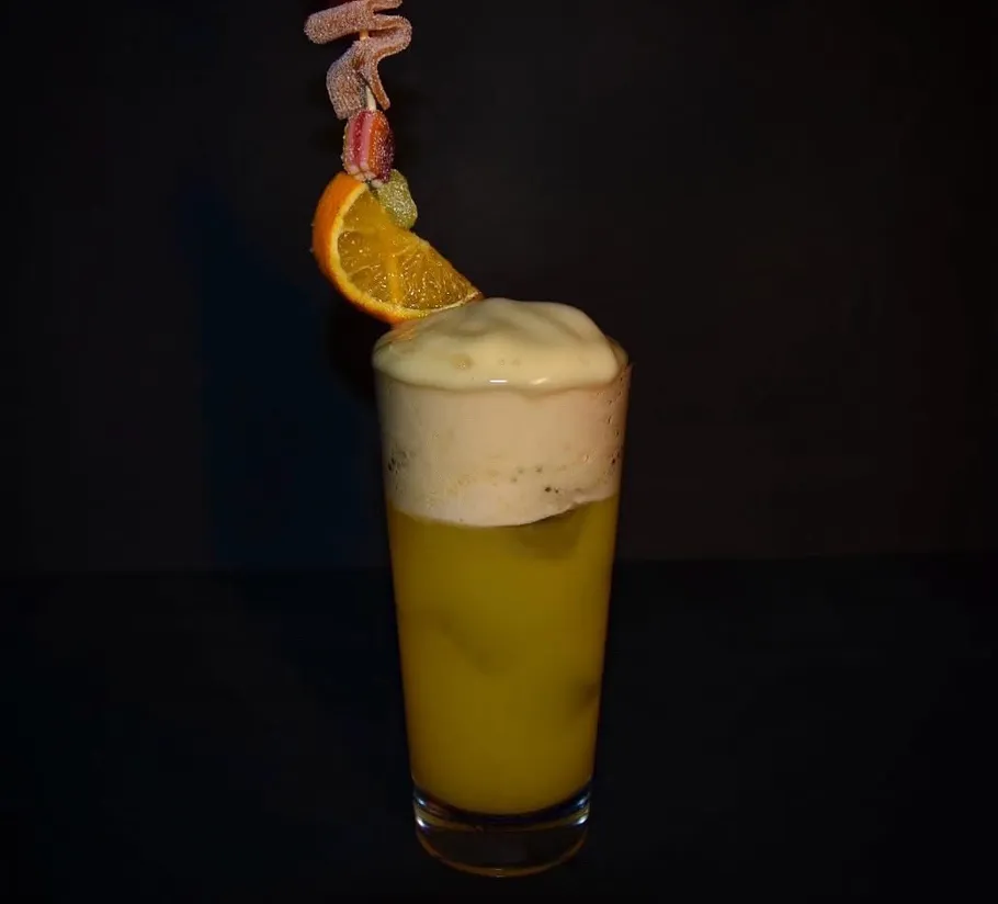 Orange cocktail with foam and fruit garnish.