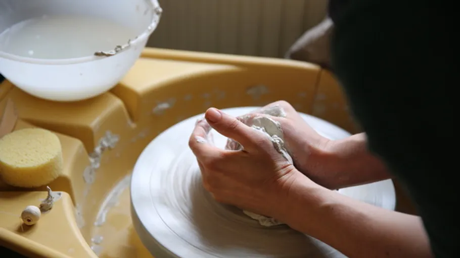 Hände formen Ton auf einer Töpferscheibe.