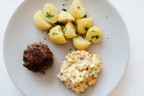 Teller mit Frikadelle, Kartoffeln und Salat.
