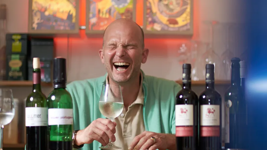 Man laughing with wine bottles on table.