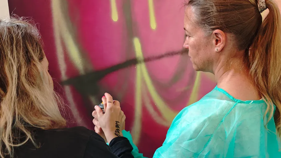 Two women spray painting a colorful wall.
