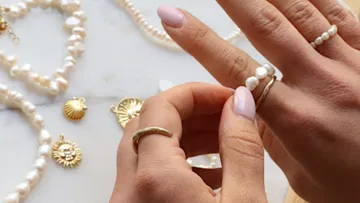 Hands wearing pearl rings with jewelry nearby.