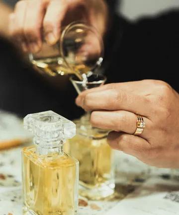 Hands pouring liquid into a small glass.