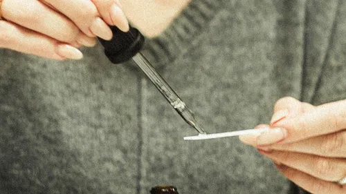 Hand nutzt Pipette auf Teststreifen, grauer Hintergrund.