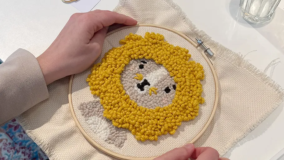 Hands holding lion punch needle art.