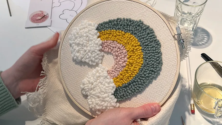 Person hält Stickrahmen mit Regenbogendesign.