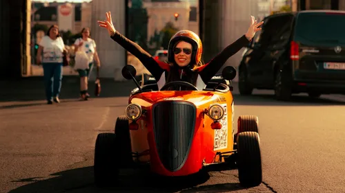 Person joyfully driving small orange car outdoors.