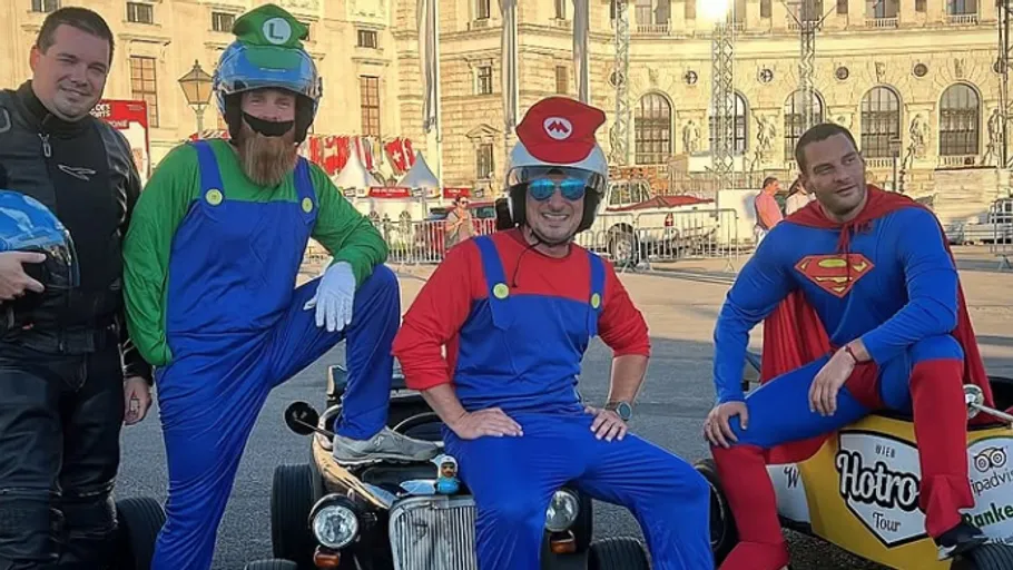 Four men in costumes with small cars, urban setting.