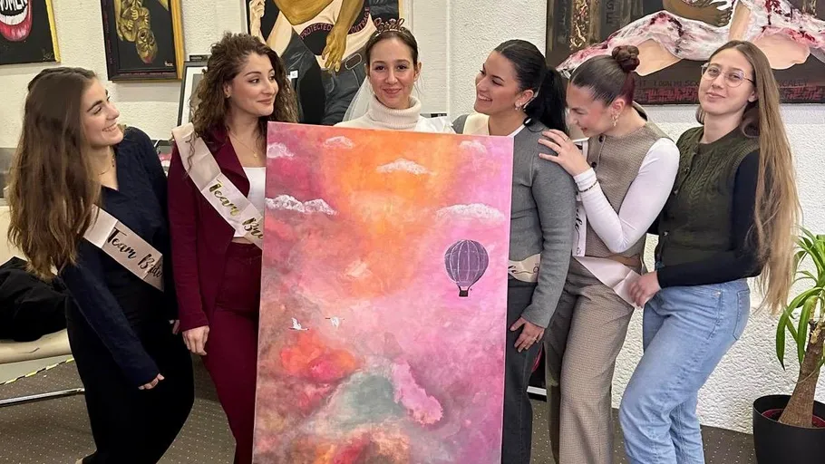 Six women holding a colorful painting indoors.