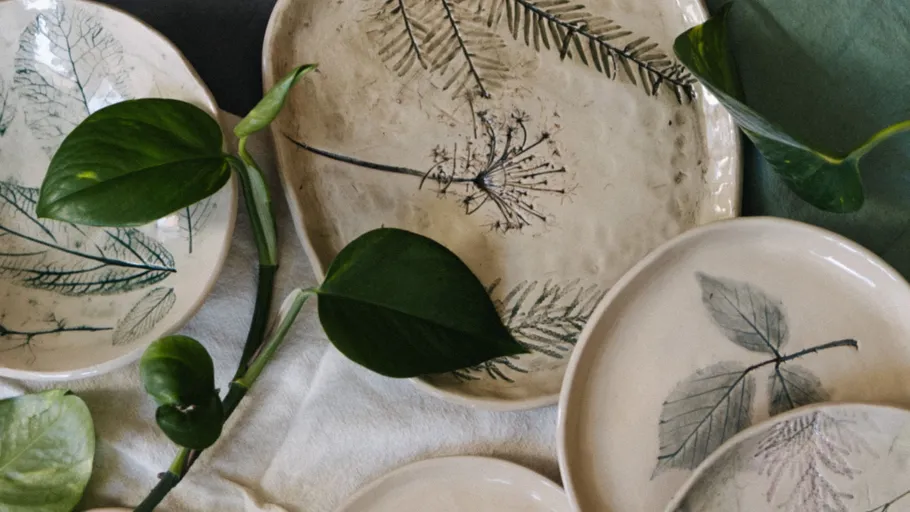 Keramikteller mit Blattmotiven und grünen Blättern.