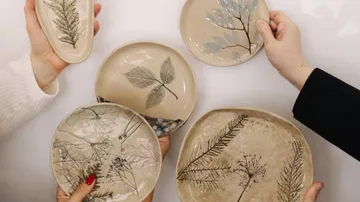 Hands holding ceramic plates with leaf designs.