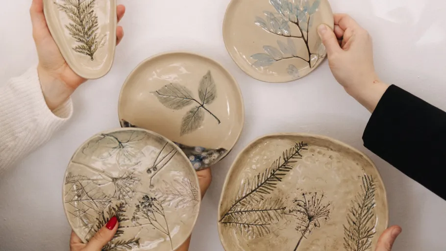 Hands holding ceramic plates with leaf designs.