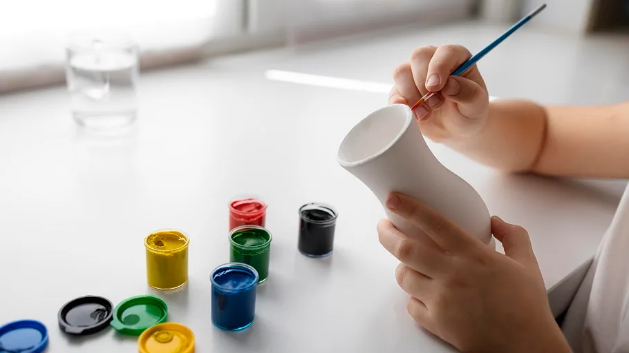 Person painting white vase with colorful paints.