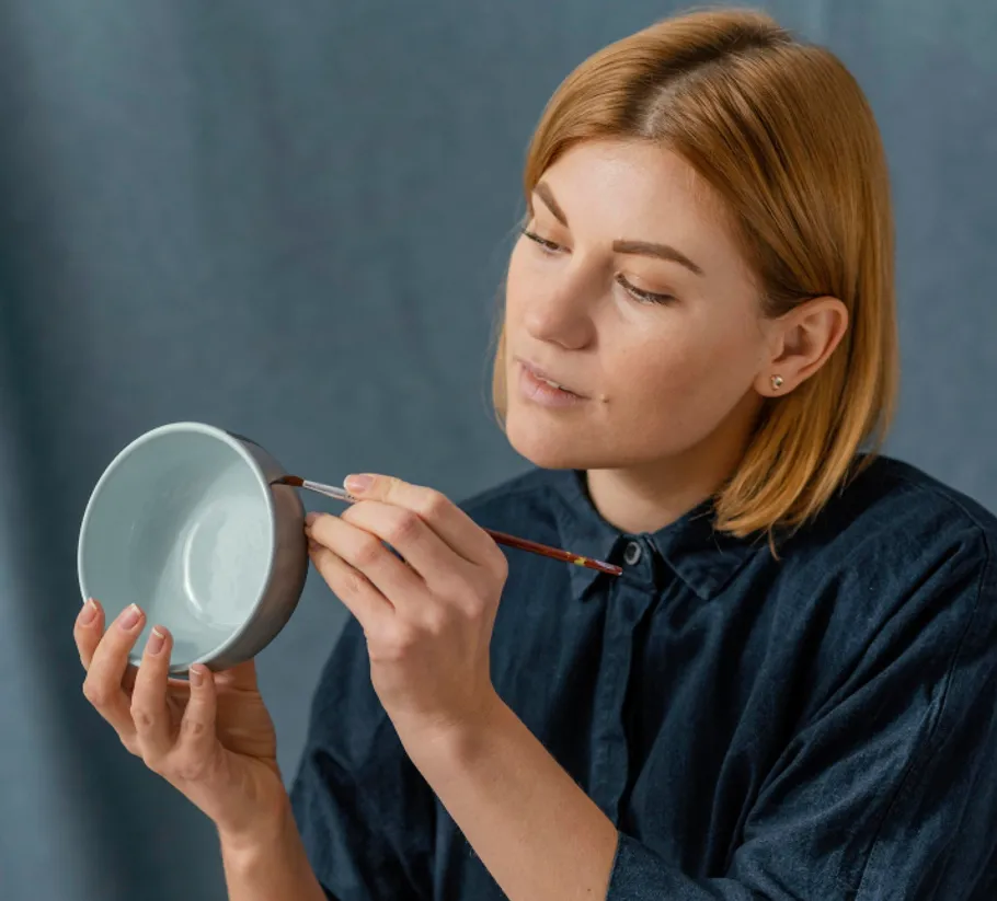 Woman painting a ceramic bowl indoors.