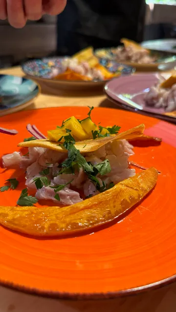 Ceviche mit Kräutern auf orangefarbenem Teller.