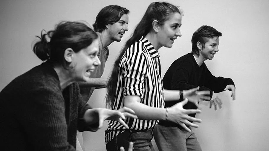 Four people enthusiastically imitating dinosaurs indoors.
