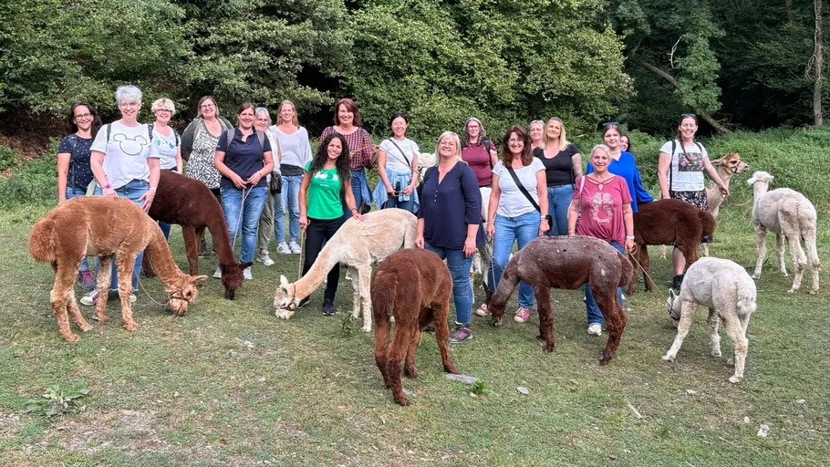 Gruppe von Frauen mit Alpakas im Wald.