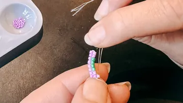 Hands crafting with purple and green beads.