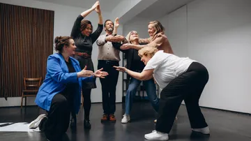 Gruppe von Menschen probt Theater in einem Raum.
