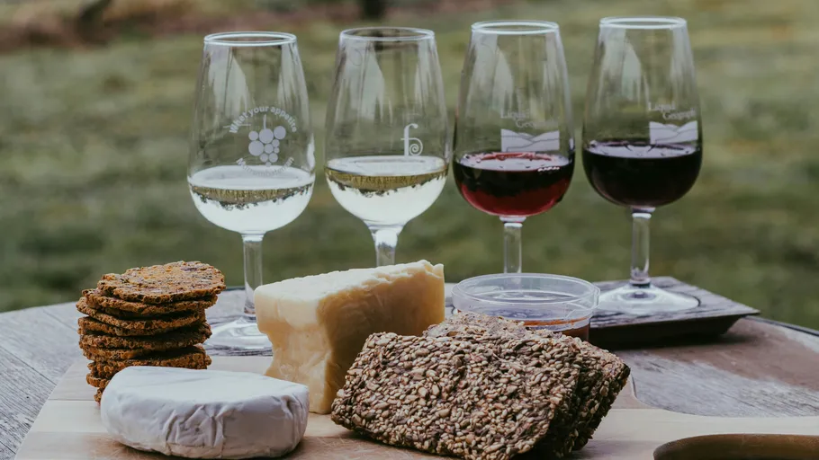 Vier Weingläser mit Käse und Crackern im Freien.