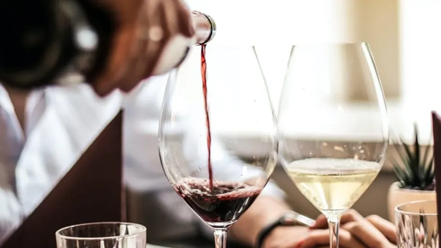 Red wine being poured into glasses, dining setting.