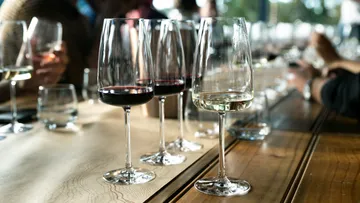 Wine glasses on wooden table, people in background.