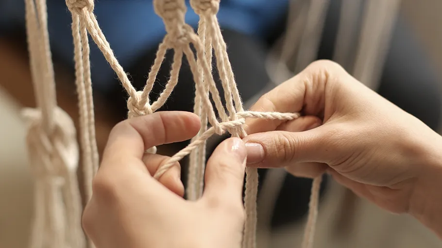Hands crafting beige macramé in close-up.